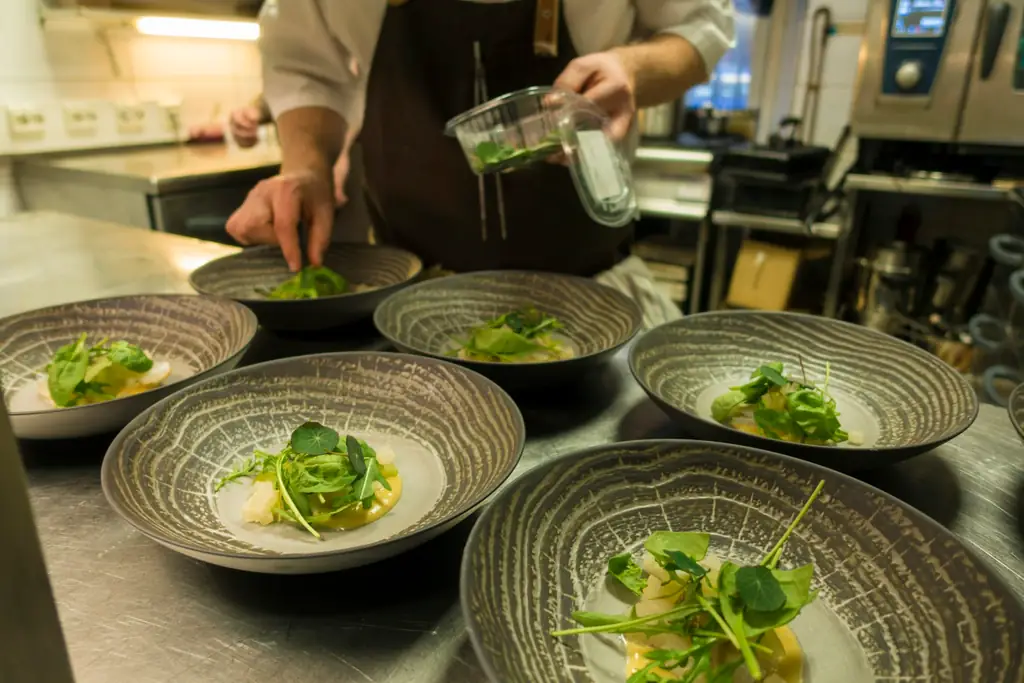 Un cocinero emplata varios cuencos en el pase de una cocina profesional.