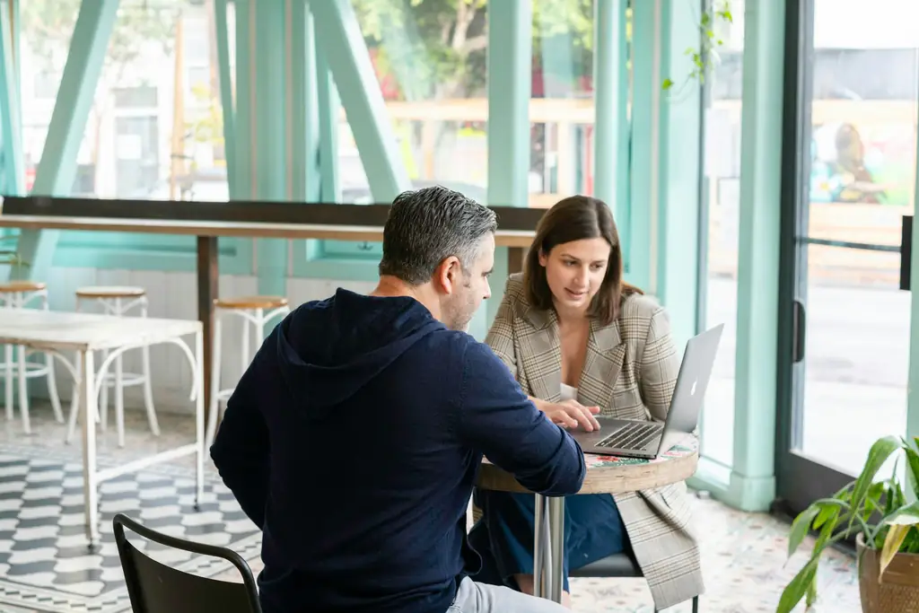 Dos personas trabajan con un portátil en la mesa de una cafetería.